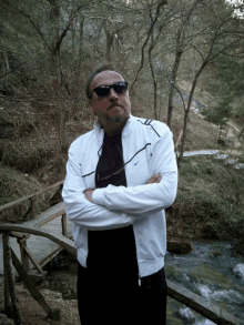 a man wearing sunglasses and a white nike jacket stands on a wooden bridge