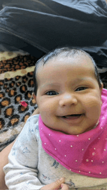 a baby wearing a pink bib is smiling and looking at the camera