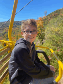 a young boy wearing glasses sits in a ski lift