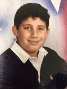 a young boy wearing a polo shirt and a black sweater smiles for the camera