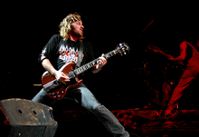 a man playing a guitar with a shirt that says ' almost dead '