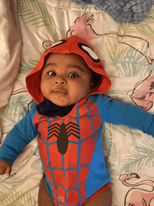 a baby in a spiderman costume is laying on a blanket