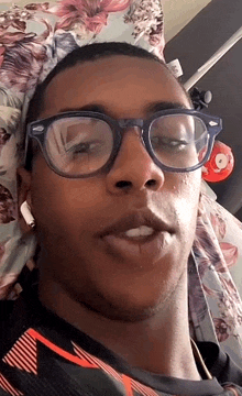 a man wearing glasses and a floral shirt is laying on a bed .