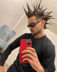 a man wearing sunglasses and a mohawk is taking a selfie with his phone .