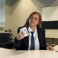 a woman in a suit and tie holds a coffee mug that says work bee ever