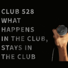 a hand is holding a microphone in front of a sign that says club 528