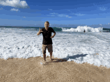 a man in a black shirt is standing on the beach giving a thumbs up