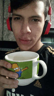 a young man wearing headphones is holding a cup of coffee with bart simpson on it