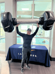 a man holding a large inflatable dumbbell in front of a la fitness table cloth