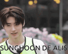 a young man wearing a yellow vest with the words sunghoon de alis on the bottom