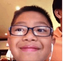 a young boy wearing glasses and ear buds is smiling and making a funny face .