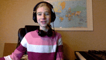 a girl wearing headphones and a pink and white striped sweater stands in front of a map of the world