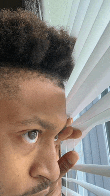 a close up of a man looking out a window through blinds