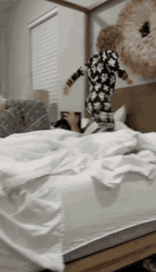 a little boy jumping on a bed with a teddy bear in the background