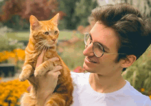 a man wearing glasses holds an orange cat