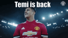 a man in a red chevrolet jersey stands in a stadium with the words " temi is back " above him