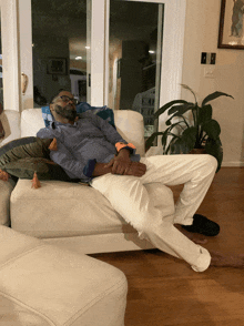 a man is laying on a white couch with a plant in the background