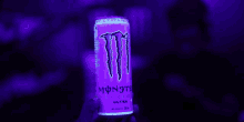 a person is holding a can of monster energy drink in a dark room .