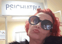 a woman wearing sunglasses is standing in front of a sign that says ' psychiatria ' on it