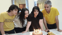 a man wearing a yellow shirt that says 882 travel is standing next to a family blowing out candles on a cake