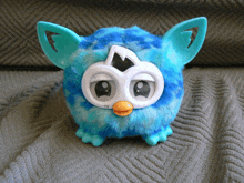 a blue furby toy is sitting on a gray blanket