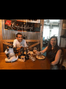 a man and woman sit at a table with a sign that says congratulations 20