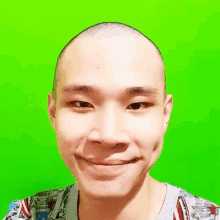 a young man with a shaved head is smiling in front of a green background