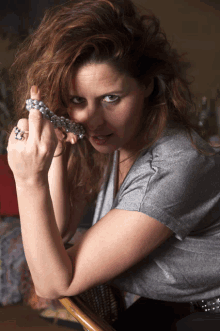 a woman in a gray shirt is holding a silver necklace in her hand