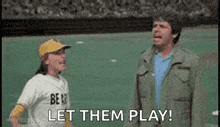 a man and a boy are standing on a baseball field . the boy is wearing a bear jersey .