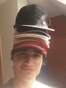 a man with a stack of hats on his head including a new era hat