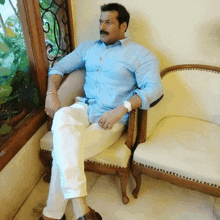 a man in a blue shirt and white pants sits on a chair