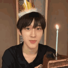 a young man wearing a party hat is sticking his tongue out in front of a cake with candles .