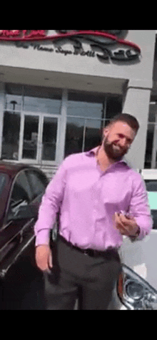 a man in a pink shirt and black pants is standing in front of a car dealership