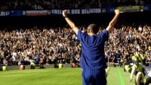 a man stands on a soccer field with his arms in the air in front of a banner that says " chelsea our religion "