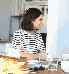 a woman in a striped shirt sits at a table with glasses of water and a box that says ' cactus '