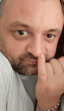 a man with a beard is holding his finger to his nose