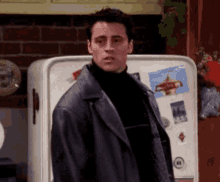 a man in a leather jacket is standing in front of a white refrigerator .