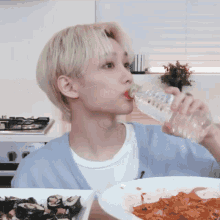 a young man is drinking water from a plastic bottle while sitting in front of a plate of food .