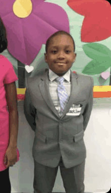 a young boy in a suit and tie is standing in front of a wall with flowers .