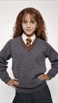 a young girl is wearing a sweater and tie and standing with her hands on her hips .