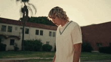 a man in a white shirt is standing in front of a building with a palm tree in the background