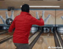 a man in a red jacket is throwing a bowling ball in a bowling alley with a state farm logo in the background