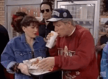 a man in a baseball cap is eating a hamburger while a woman in a denim jacket holds a tray .