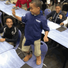 a boy wearing a blue shirt that says ' brooklyn ' on it stands in front of a classroom full of children