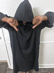 a person wearing a black robe with a hood is giving a thumbs down