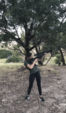 a woman holding a rifle in front of a tree in a field