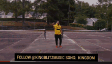 a man in a yellow shirt is standing on a tennis court with the words follow @kingblitzmusic song kingdom below him