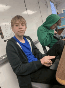 a boy wearing a green hoodie sits at a desk