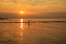 a sunset over a body of water with a person on a paddle board