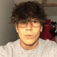 a young man wearing glasses and a grey sweater takes a selfie